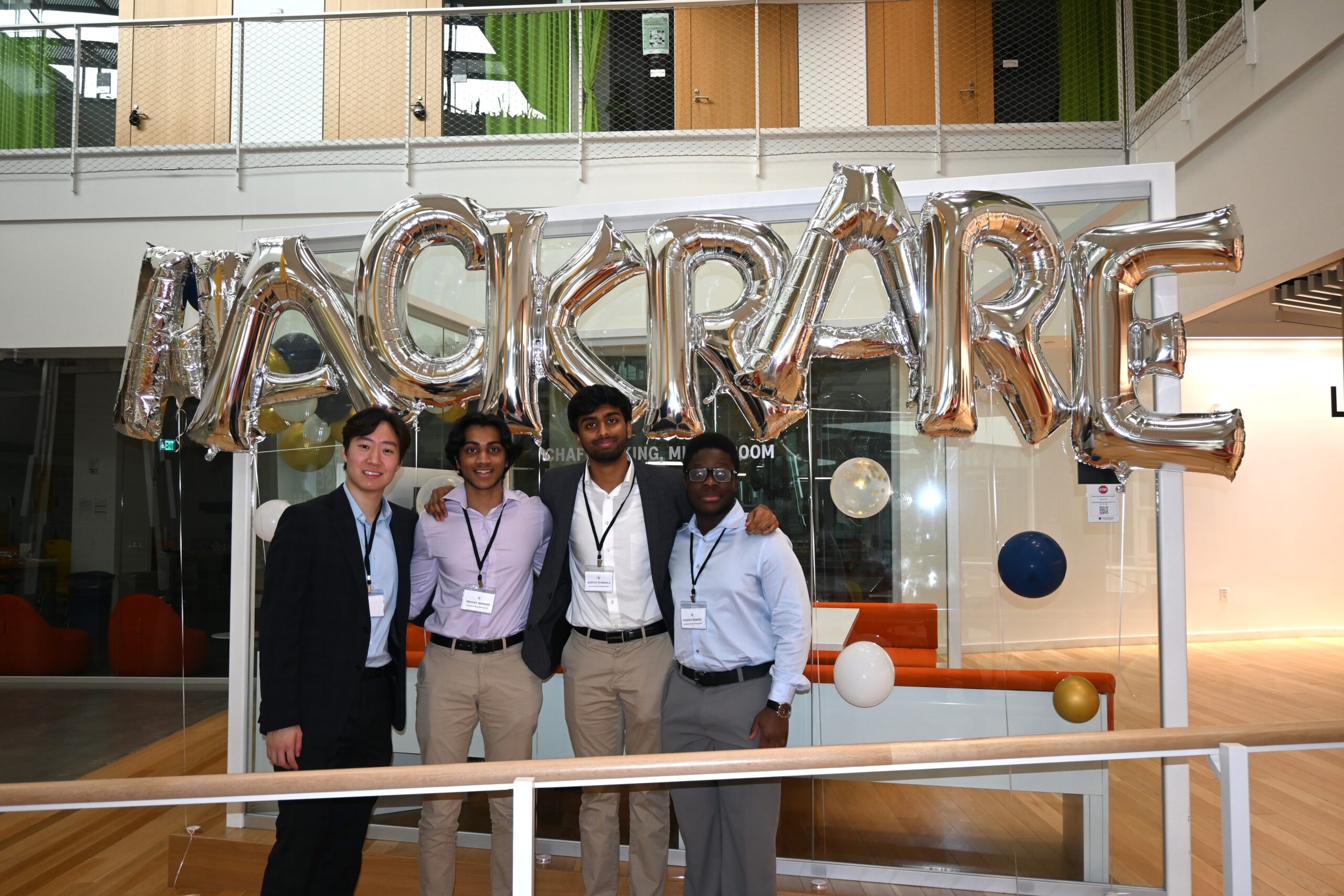 The authors, a Harvard Rare Disease Hackathon team, posing together in front of balloons that say "HACK RARE"