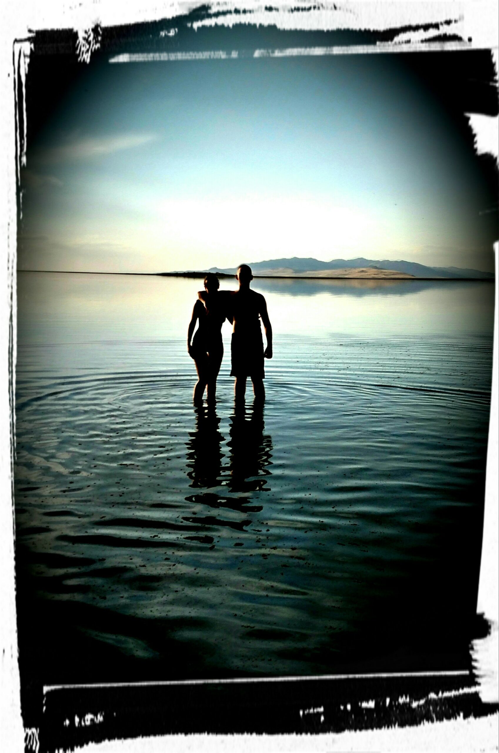 Photo of mother and son in silhouette wading into the ocean