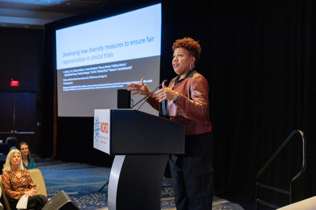A presenter on stage at a NORD event speaking at the podium about their clinical trial insights